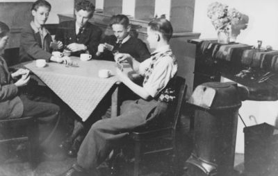 876576 Portret van vijf jongens die aan het kaarten zijn aan een tafeltje in zaaltje van het St. Franciscushuis ...